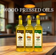 Three Maagaani wood-pressed oil bottles — groundnut, sunflower, and sesame — displayed on a wooden kitchen counter with a warm, rustic background.