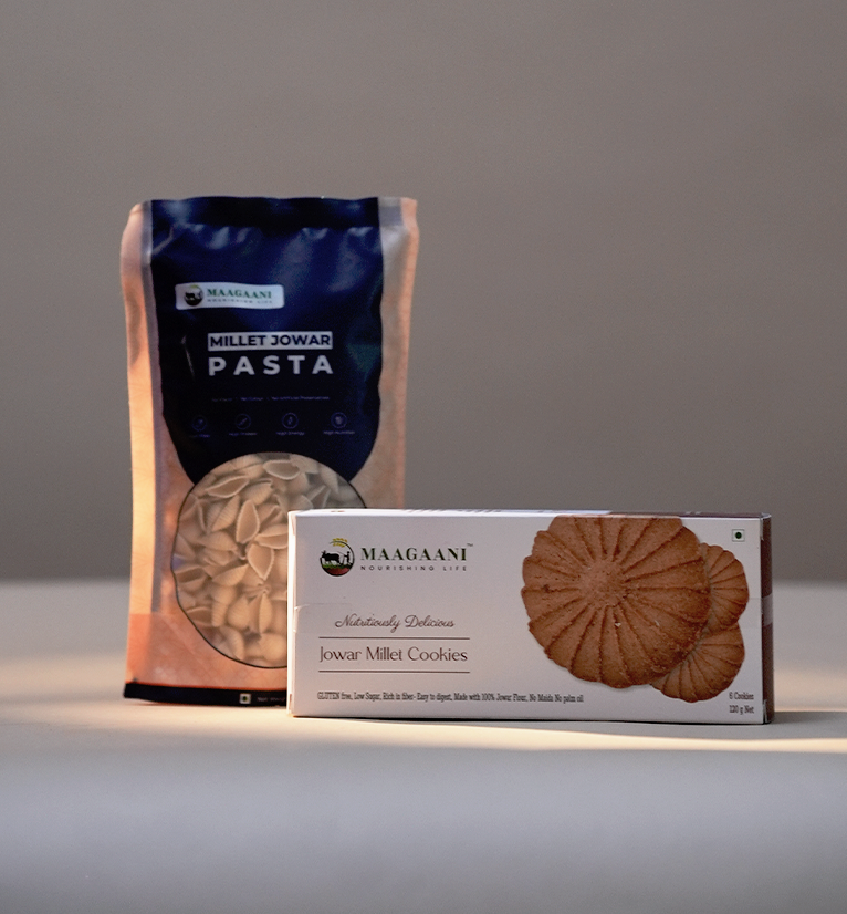 Packaged Jowar Millet Pasta and Jowar Cookies displayed on a table, with the brand name visible on the packaging.